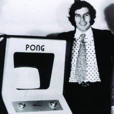 nolan bushnell standing next to a pong arcade machine